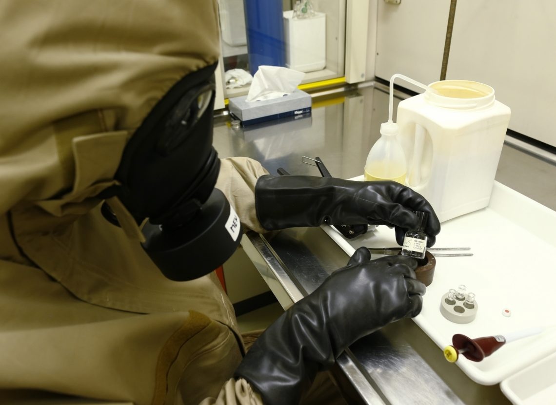 Une personne en tenue de protection, assise à un établi de laboratoire, tient une petite bouteille entre ses mains