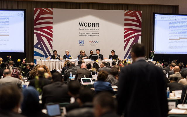 Lors d’une conférence internationale sur la protection de la population, plusieurs personnes assises sur une estrade participent à un débat public. 
