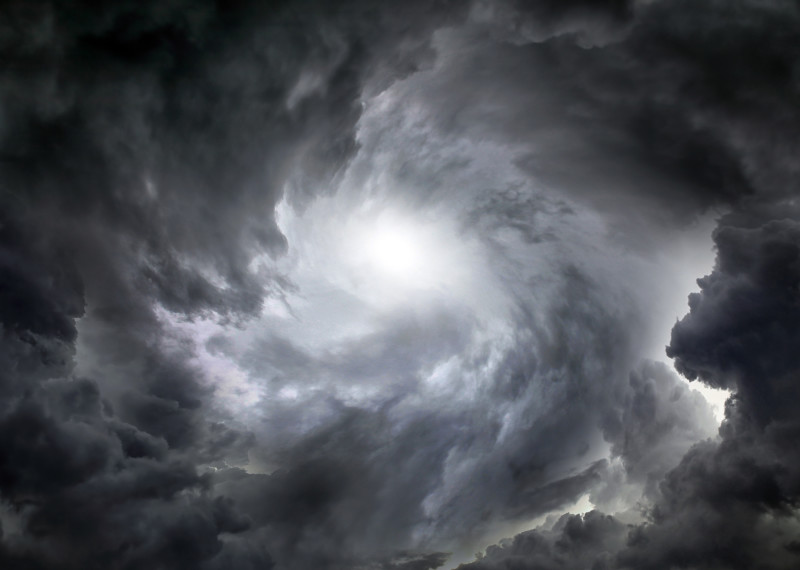 Das Bild zeigt das Auge eines Sturms. Am Rand sind dunkelgraue Wolken, die spiralförmig in die Mitte des Bildes immer heller werden. Am rechten unteren Rand ist es etwas heller, vermutlich wegen eines Blitzes. 